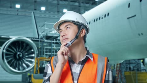 close up de ingeniero masculino asiático con casco de seguridad de pie con aviones en el hangar. pensando en algo y mirando a su alrededor mientras el mantenimiento de aviones