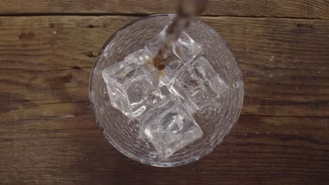 pouring beer into a transparent glass with ice cubes laying at the bottom