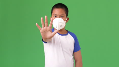 young boy wearing pollution mask showing stop sign on a green screen