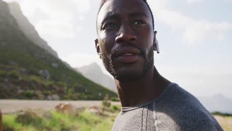 african american man listening to music putting earphones in while exercising in countryside