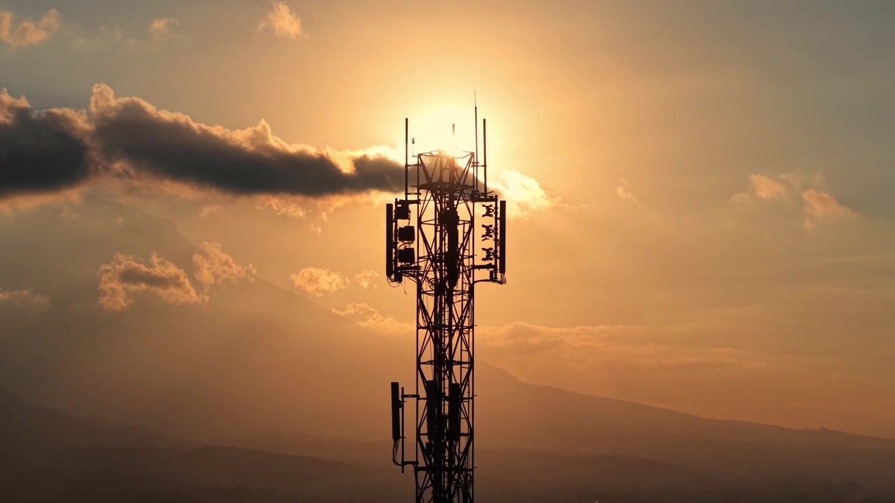 Silhouette of cellular tower against golden sunset sky. Telecommunication, network, and technology concept, dramatic evening cloudy background footage.