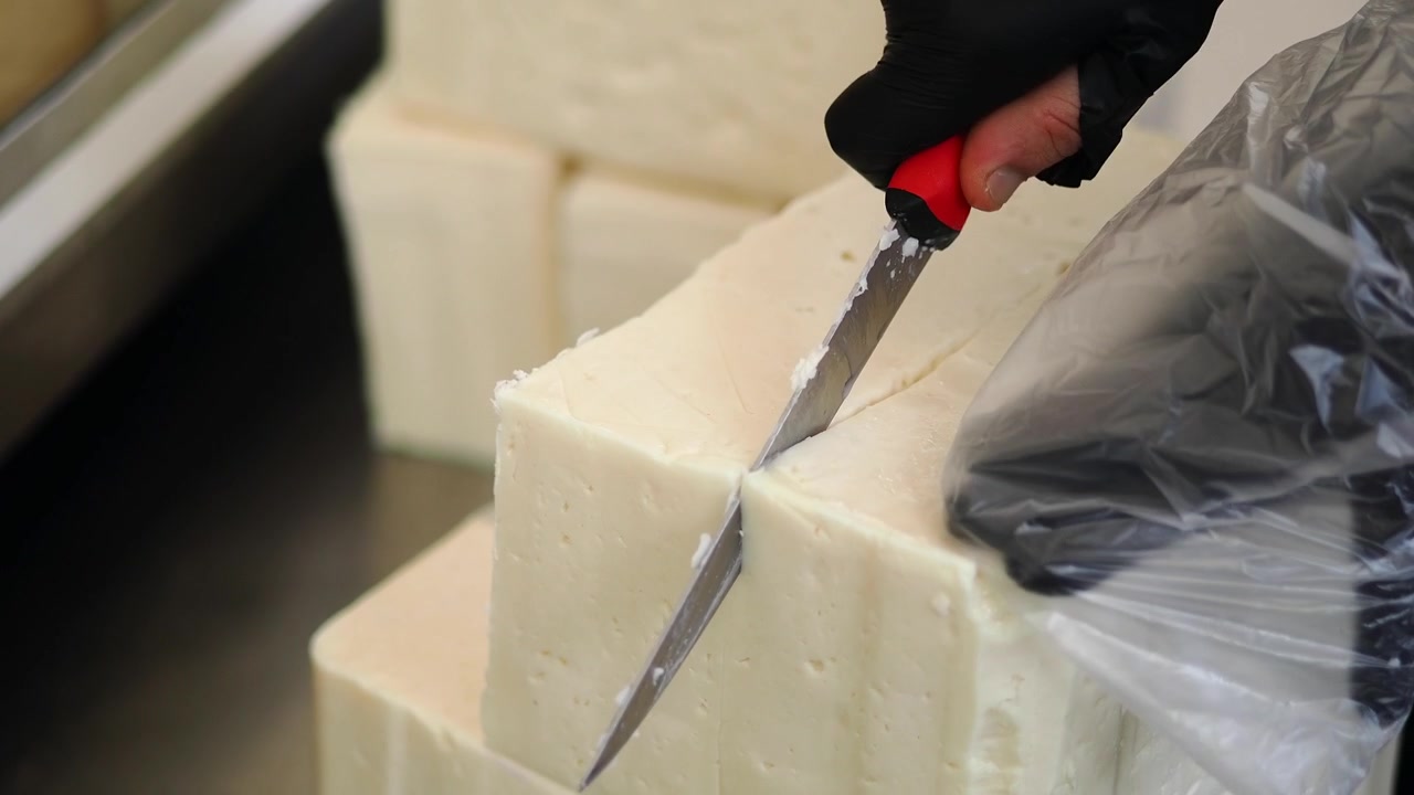 Person Cutting Large Block of White Cheese in a Kitchen