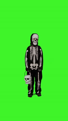 video vertical de larga duración de un niño vestido con un disfraz de esqueleto llamando a la puerta truco o trato en halloween sosteniendo un cubo en forma de calabaza jack o'lantern contra la pantalla verde del estudio 1