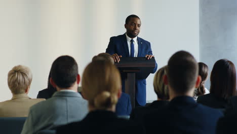 vista trasera de personas sentadas en una sala de conferencias que escuchan a un hombre de negocios afroamericano hablando con confianza y emoción