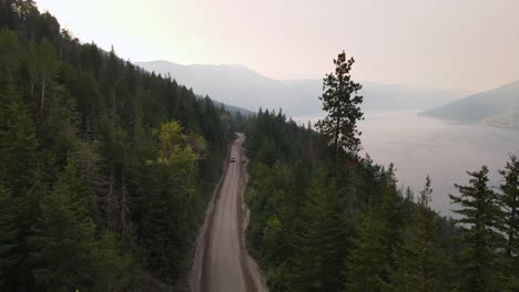 Pick-up-truck-passing-a-parked-car-along-a-dirt-road-that-leads-through-British-Columbia's-vast-coniferous-forests