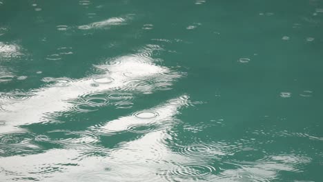 tropical summer rain splashing into swimming pool. close up of swimming pool during storm and rain drops falling into water.