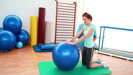 trainer helping his client stretch her back with exercise ball