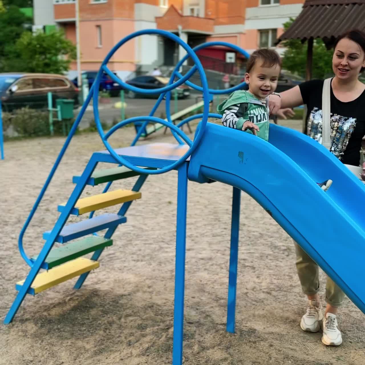 Caring mom holding her child sliding on the playground. Happy baby having good time outdoors. Vertical video