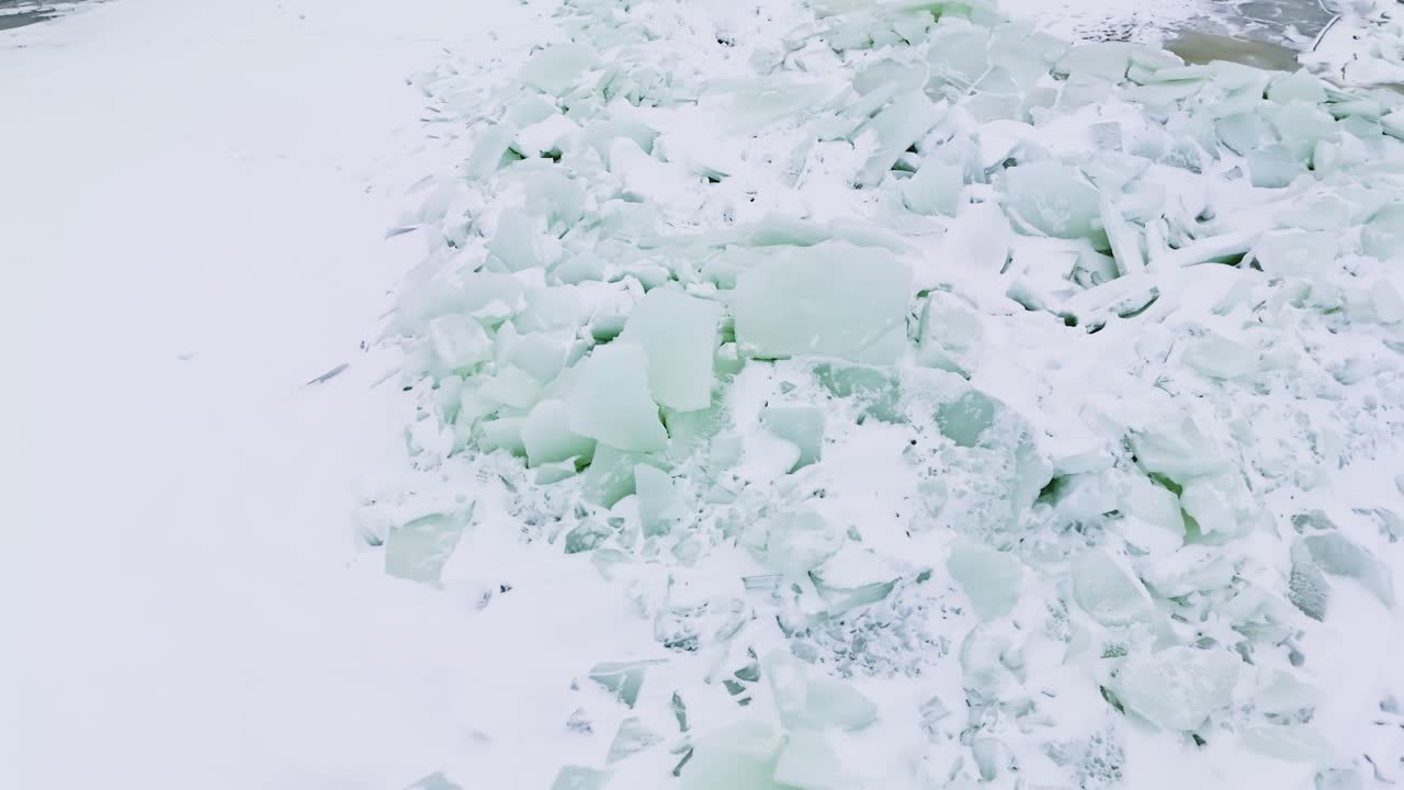 Primo piano con drone di banchisa frantumata accumulata in una cresta di pressione su un mare ghiacciato, placche turchesi pallide e neve che creano una trama invernale astratta
