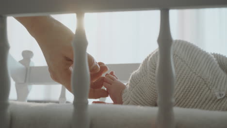 mother's hand touches baby's feet in crib