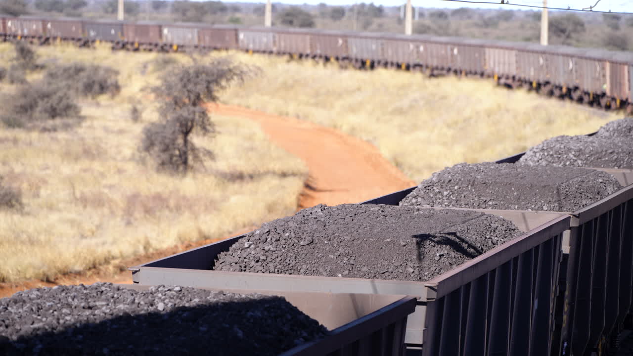Multiple train wagons of mined manganese ore moving slowly in the South African bush outback