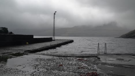 Panning-shot-of-Foroyar-Pier-in-Funningur-town-during-grey-cloudy-day-on-Eysturoy-Island