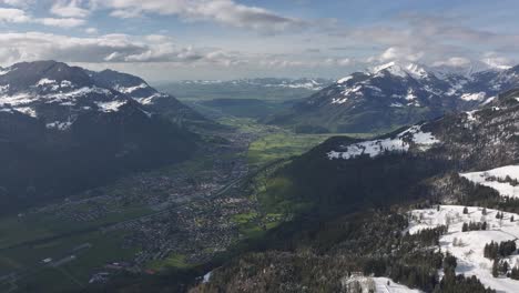 Aerial-perspective-of-a-valley-nestled-in-Glarus,-Switzerland,-encircled-by-snow-capped-mountain-ranges,-showcasing-the-captivating-allure-of-the-Swiss-Alps