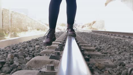 Young-woman-with-purple-boots-tries-to-maintain-balance-on-the-train-tracks,-but-fails