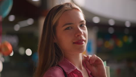 la dama de vestido rosa mira con confianza a la cámara con una sonrisa encantadora. coloca suavemente su bolsa de compras detrás de ella mientras que, estructuras poco claras y luces borrosas llenan el fondo