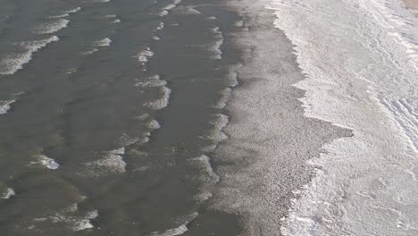 gentle waves lapping onto a sandy shore, sunlight reflecting on water, aerial view