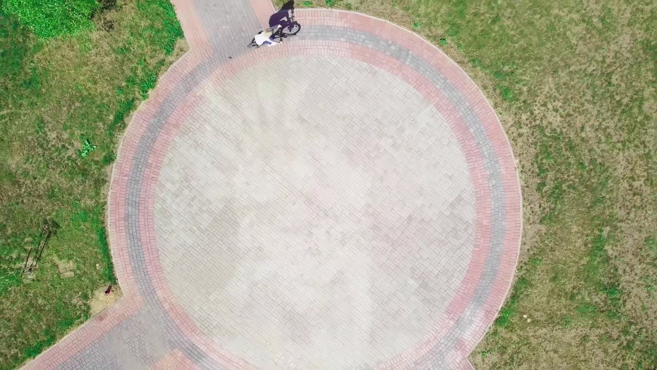 vista superior de una mujer en bicicleta montando una bicicleta en una carretera circular en un parque de la ciudad.