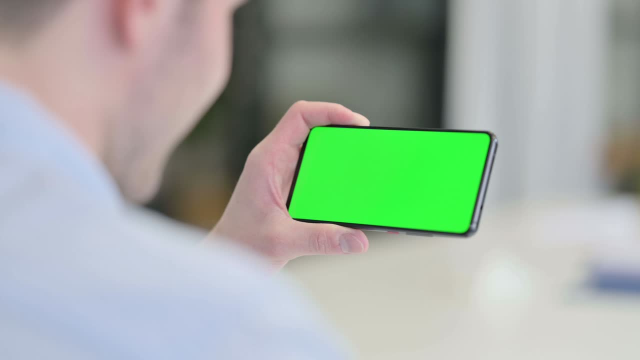 크로마 스크린 을 가진 스마트폰 을 보고 있는 젊은 남자 의 뒷면