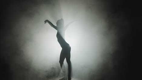 modern ballet performance. silhouette of graceful ballerina dancing in textured smoke in spotlight on stage