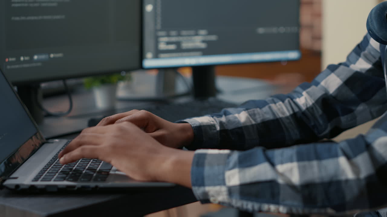 Closeup of programer hands typing machine learning code on laptop keyboard in front of computer screens