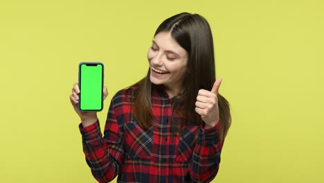 mujer sonriente señalando con el dedo la pantalla verde del teléfono inteligente mostrando los pulgares hacia arriba