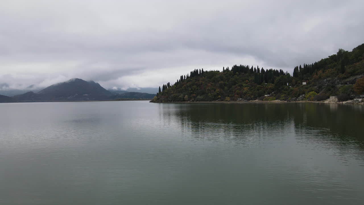 몬테네그로의 깨끗한 호수 옆에 있는 멀고 어둡고 외로운 섬 위로 폭풍 구름의 드론 샷