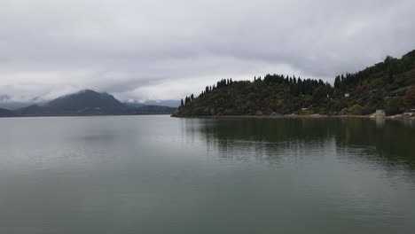 Drone-shot-of-storm-clouds-over-a-distant,-dark,-lonely-island-beside-the-pristine-lake-in-Montenegro