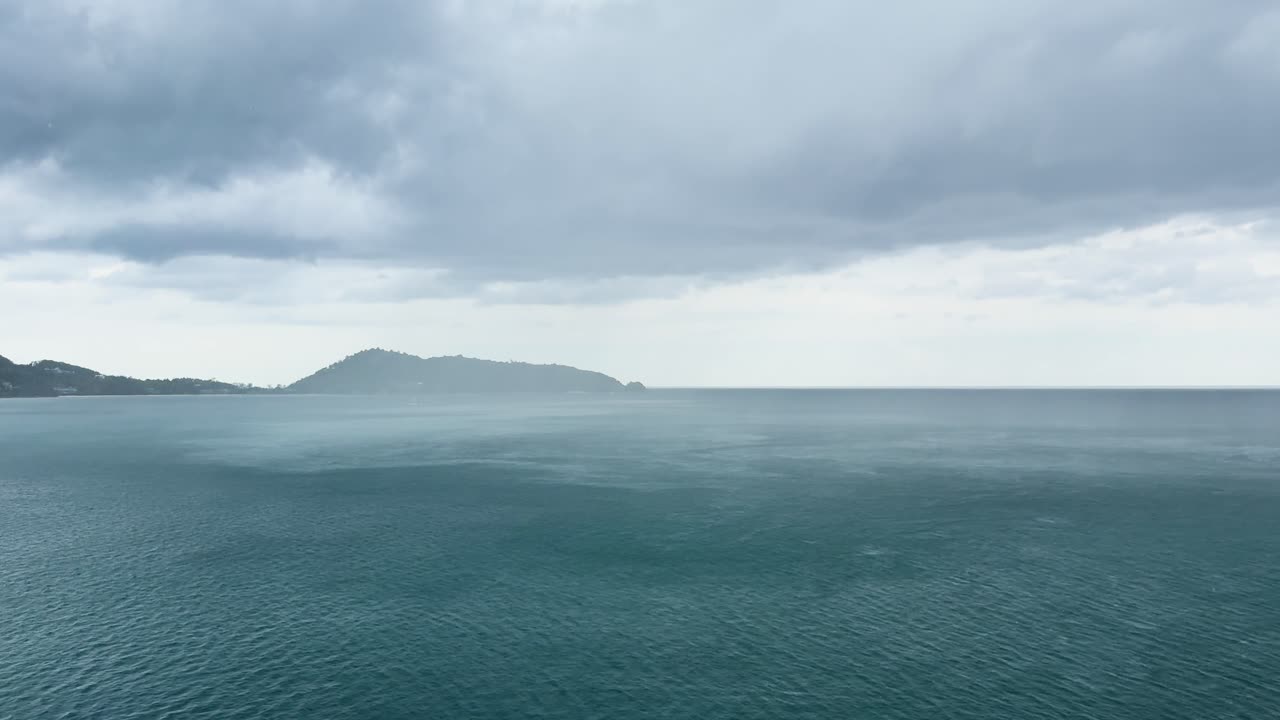 Dramatic storm clouds gather over Kalim Beach, Phuket, with turbulent ocean waves and shifting light creating a moody atmosphere