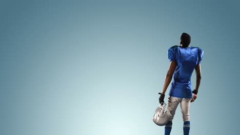 Rear-view-of-male-rugby-player-wearing-holding-helmet-and-rugby-ball-against-blue-background