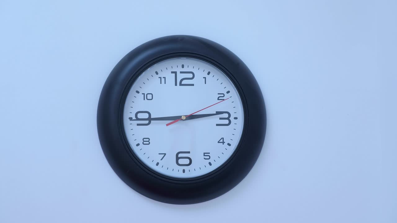 Black circle wall clock beginning on white wall background. 9:13 time.