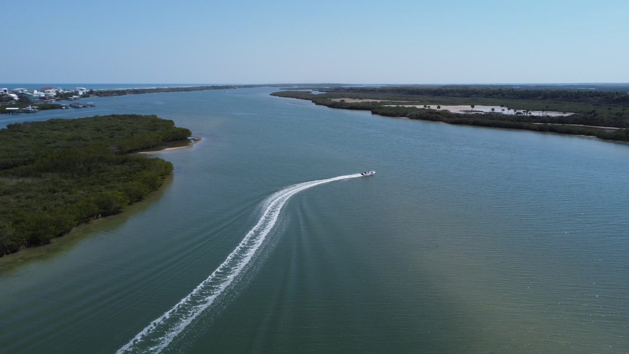 Drone following a high-speed boat leaving a wake on the water on a beautiful lake next to the beach in New Smyrna Beach, Florida