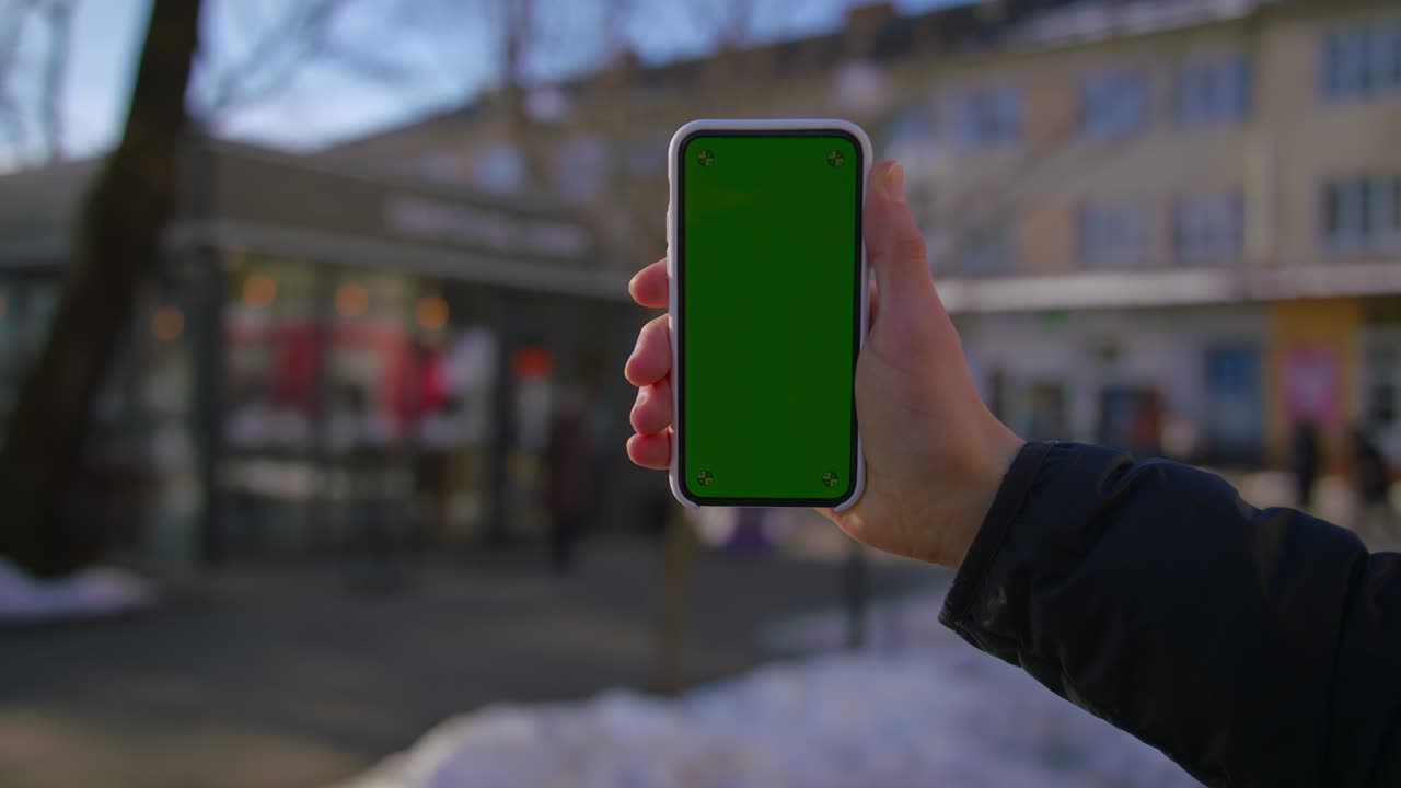 Hand man uses holding a mobile telephone with a vertical green screen background on of street houses people key smartphone technology touch message display