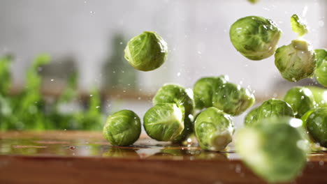 slow motion of fresh brussels sprouts falling on wet wooden board in a kitchen