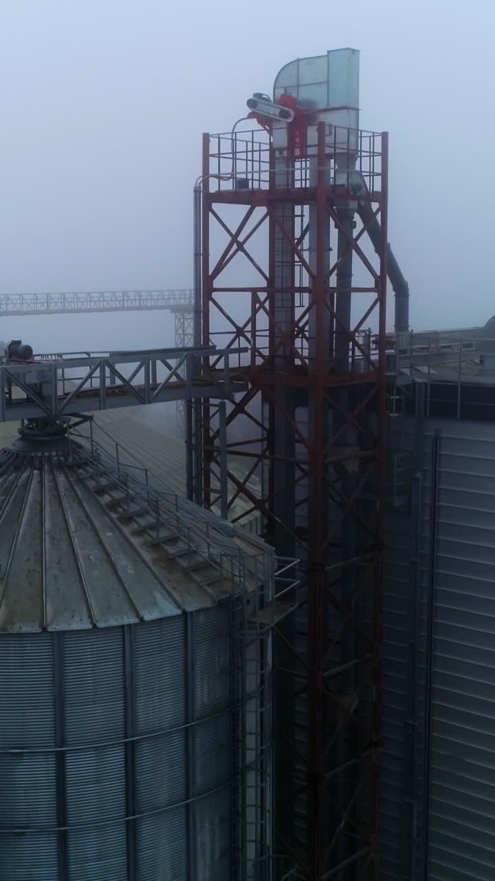 Grain containers and warehouses at the present day elevator complex. Huge silo premises in the foggy weather day. View from above. Vertical video