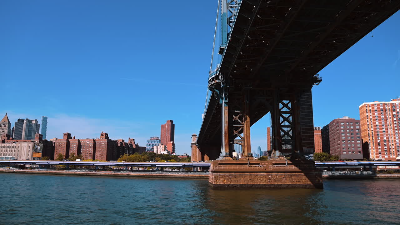 Passaggio sotto il Ponte di Manhattan lungo l'East River. Vista sullo skyline di New York in una giornata di sole limpida dal fiume.