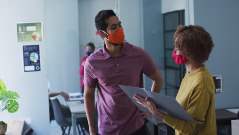 Mixed-race-man-and-woman-wearing-face-masks-in-office