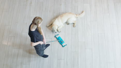 teenage girl cleaning the floor with a mop while a golden retriever dog is resting on the floor