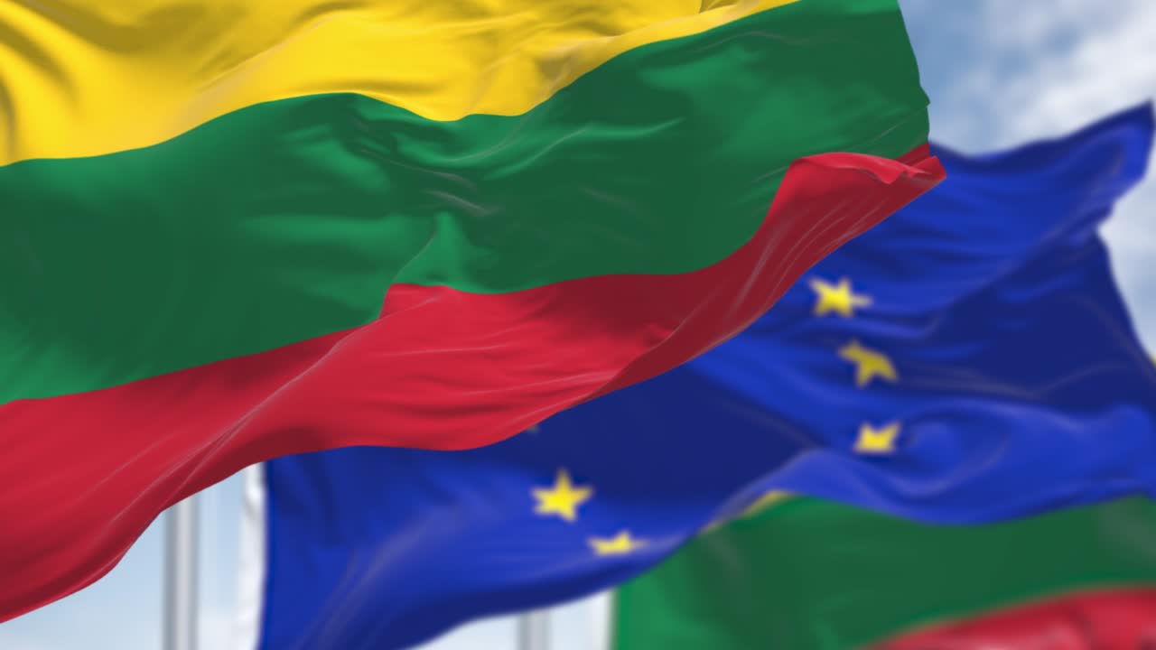 리투아니아의 국기가 바람에 흔들리고, 배경에는 유럽연합의 발이 흐려져 있다.