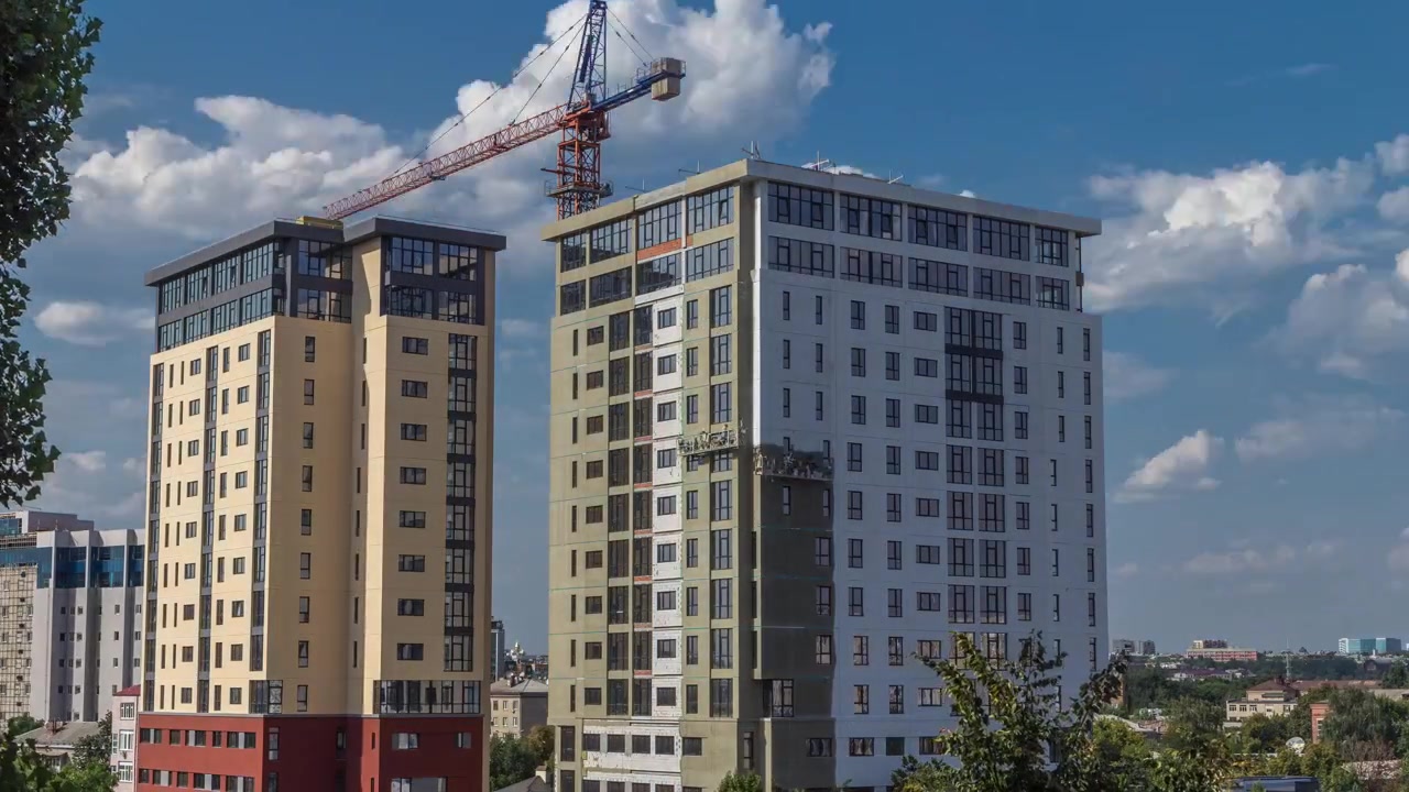 Kran og byggeplads mod blå himmel, luftfoto timelapse. Arbejdere maler vægge i et nyt beboelsesejendom.