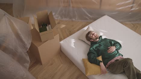 man relaxing on mattress in new apartment during moving