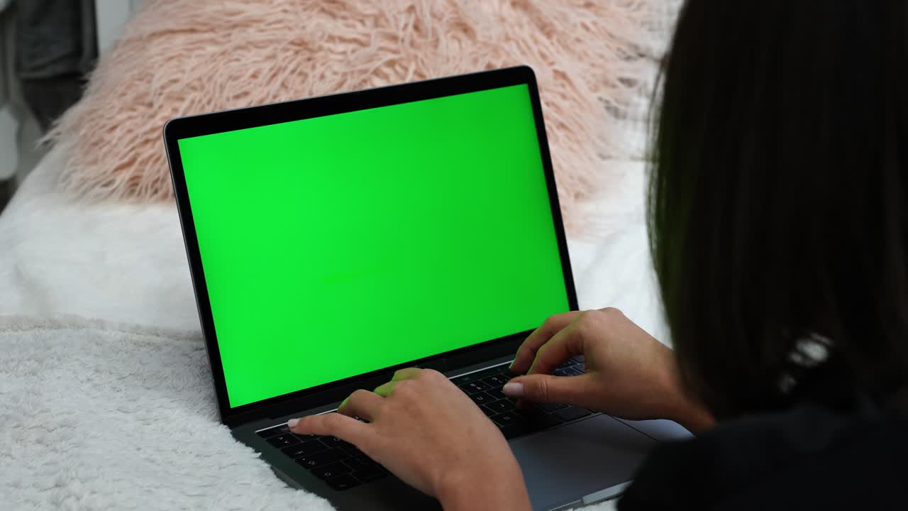 mujer escribiendo en una computadora portátil con pantalla verde mientras está acostada en la cama, blogueando o concepto de programación