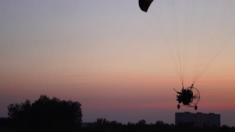 el piloto en un parapente vuela desde la cámara moviéndose gradualmente hacia la distancia contra el hermoso cielo al atardecer.