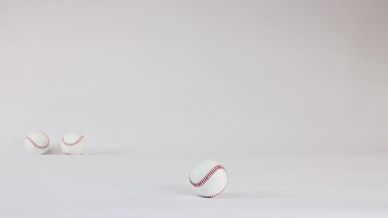 Tre vita basebollar med röda sömmar studsar och rullar över ett ljust vitt studiogolv