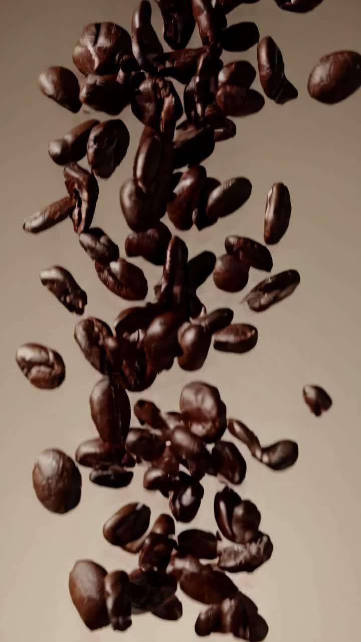 Video ravvicinato di chicchi di caffè che cadono su uno sfondo beige, ripreso dal basso