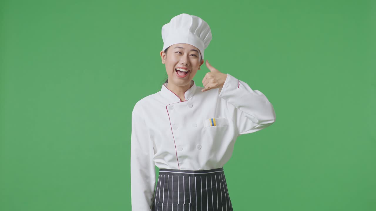 Asian Woman Chef Smiling And Making Call Me Gesture To Camera While Standing In The Green Screen Background Studio