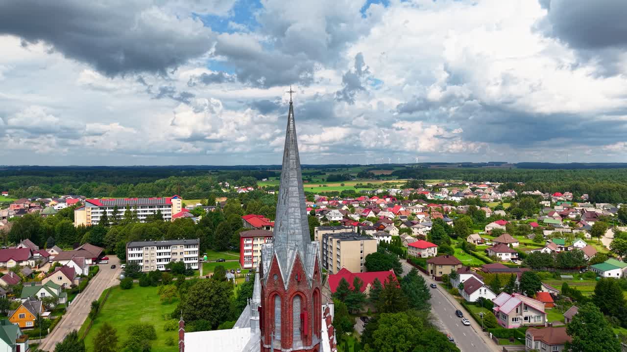 Aerial close-up of Šilalė St. Francis of Assisi Church spire with dramatic clouds and surrounding Lithuanian townscape and countryside in view
