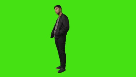 full length shot of smiling casually dressed young man standing against green screen folding arms and putting hands in pockets 1