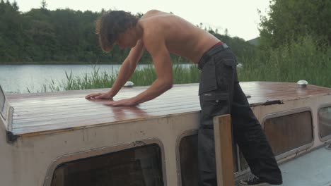 topless joven carpintero lijado a mano tablones de techo de barco de madera con papel de lija