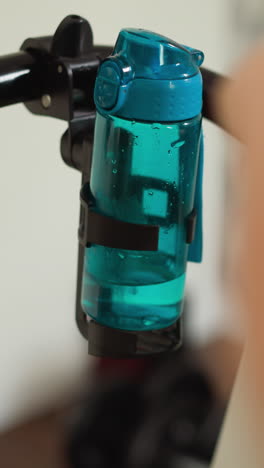 botella de agua en el soporte de la cinta de correr en el hogar de cerca. bebida refrescante para la mujer haciendo ejercicio cardio duro con la máquina en la casa. mantener hidratado haciendo ejercicio