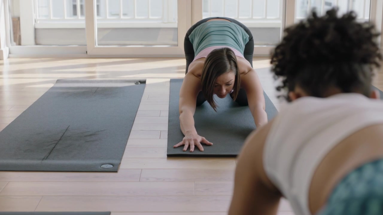 Starting stretch, woman in teal tank top sliding hands forward yoga mat at studio, natural light